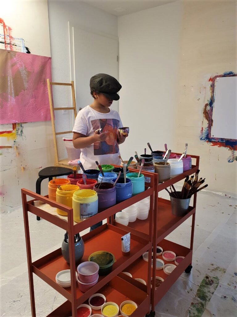 Kind im Malatelier stehend an der Malfarbenpalette.